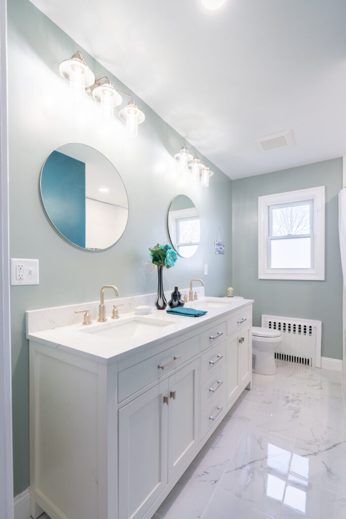 Modern bathroom remodel with double vanity, quartz countertop, round mirrors, and marble-look tile flooring.
